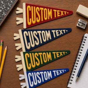 May include: Four triangular felt pennants featuring embroidered text. The top is red with yellow text, the second is navy with cream text, the third is dark green with yellow text, and the bottom is light blue with white text. Each reads CUSTOM TEXT.