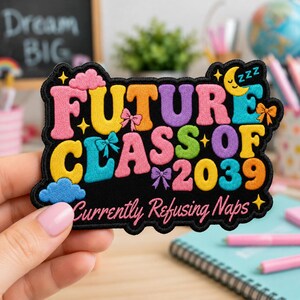 May include: A black embroidered patch featuring the colorful text FUTURE CLASS OF 2039 and Currently Refusing Naps. The design includes pink and blue clouds, a yellow crescent moon with zzz, and small purple, pink, and blue bows.