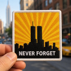 May include: A square embroidered patch featuring a black silhouette of the Twin Towers and city skyline against a yellow sunburst background. The text NEVER FORGET is stitched in white capital letters at the bottom, bordered by a white edge.