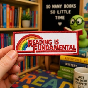 May include: A rectangular embroidered patch with a white background and a red border. It features a colorful rainbow graphic on the left and the red text Reading Is Fundamental centered on the right, with a red horizontal line underneath.