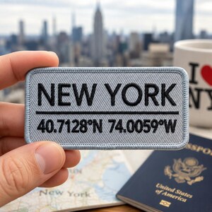 May include: A rectangular light gray embroidered patch with a stitched border. The text NEW YORK is embroidered in black on the top line, with the coordinates 40.7128°N 74.0059°W in black on the bottom line, separated by a horizontal black line.