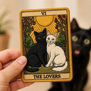 May include: A rectangular embroidered patch featuring a tarot card design titled THE LOVERS with the Roman numeral VI. The artwork depicts a black cat and a white cat sitting side-by-side in a garden under a large yellow sun and trees.