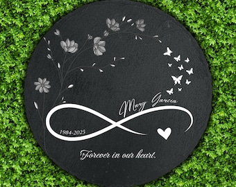 May include: A round, black memorial stone with white floral and butterfly designs. The name "Mary Garcia" is inscribed, along with the years "1984-2025" and the phrase "Forever in our heart."