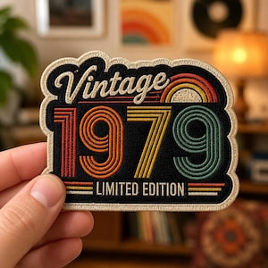 May include: An embroidered patch with a black background featuring the text Vintage 1979 Limited Edition. The design includes a retro-style rainbow arc and concentric line patterns in shades of orange, yellow, and teal, finished with a beige border.