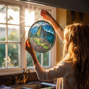 May include: A round stained glass panel depicting Machu Picchu, with a black metal frame and a hanging chain. The artwork features a detailed landscape of the ancient city, with green mountains, blue skies, and colorful details.