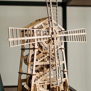 May include: A wooden windmill model with intricate gears and a ladder. The model features a tall, rectangular structure with rotating blades and detailed internal mechanisms. The text "WO Trick" is visible on the side.
