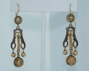 May include: A pair of gold-toned dangle earrings with a delicate chain and a round, ornate charm at the bottom.