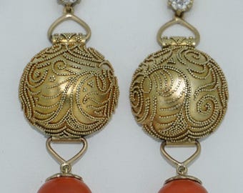 May include: A pair of gold-toned earrings. Each earring features a round, filigree-detailed pendant with an orange-red sphere dangling below. A small, clear gemstone tops each earring.