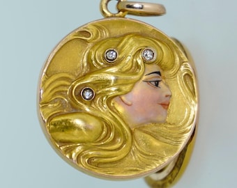 May include: A gold-colored pendant with a detailed Art Nouveau design. The pendant features a profile of a woman with flowing blonde hair, accented with three small diamonds. The woman's face is painted with delicate features.