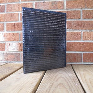 May include: A black, rectangular, reflective window screen with a grid pattern. The screen is made of a thin, flexible material and is designed to block out heat and light.