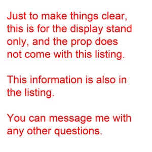 May include: White background with red text. The text reads: "Just to make things clear, this is for the display stand only, and the prop does not come with this listing. This information is also in the listing. You can message me with any other questions."