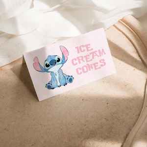 Puede incluir: Una tarjeta rosa claro con el texto "ICE CREAM CONES" y una ilustraci&oacute;n de un personaje de dibujos animados azul. La tarjeta est&aacute; sobre una superficie marr&oacute;n claro.
