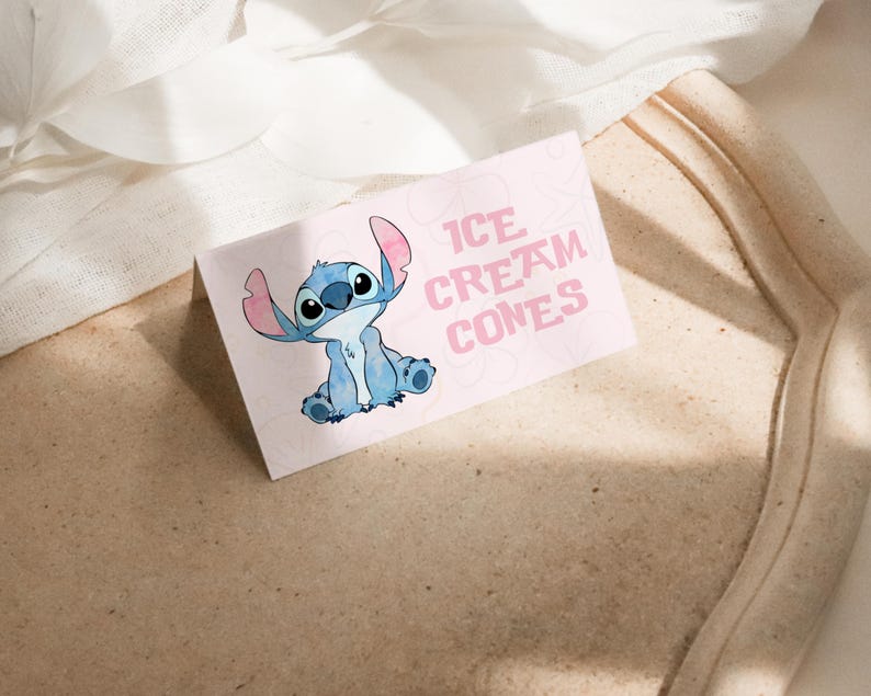 Puede incluir: Una tarjeta rosa claro con el texto "ICE CREAM CONES" y una ilustraci&oacute;n de un personaje de dibujos animados azul. La tarjeta est&aacute; sobre una superficie marr&oacute;n claro.
