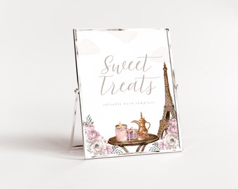 May include: A clear acrylic sign displaying "Sweet Treats" in cursive script. The sign features illustrations of the Eiffel Tower, a table with a teapot, candles, and floral accents. The sign is set against a white backdrop.