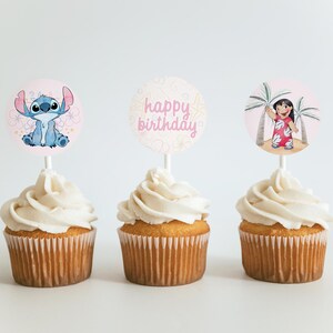 Puede incluir: Tres cupcakes con glaseado blanco y adornos. Uno presenta a Stitch, otro dice "feliz cumplea&ntilde;os" y el tercero muestra a una ni&ntilde;a con palmeras. Los cupcakes tienen envoltorios de papel marr&oacute;n.