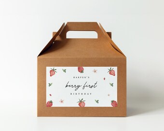 May include: A brown cardboard gift box with a handle. The box features a white label with the text "Harper's berry first BIRTHDAY" surrounded by watercolor strawberries and leaves. Perfect for a first birthday celebration.