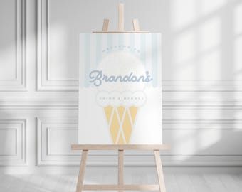 May include: A light blue and white ice cream-themed birthday sign on a wooden easel. The sign reads "Welcome to Brandon's Third Birthday" in a playful font, with an ice cream cone illustration.