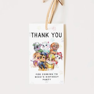 Puede incluir: Una etiqueta de regalo blanca con el texto "THANK YOU" en la parte superior y "FOR COMING TO BEAU'S BIRTHDAY PARTY" en la parte inferior. La etiqueta presenta una colorida ilustración de cachorros de dibujos animados. Una cuerda marrón está unida en la parte superior.