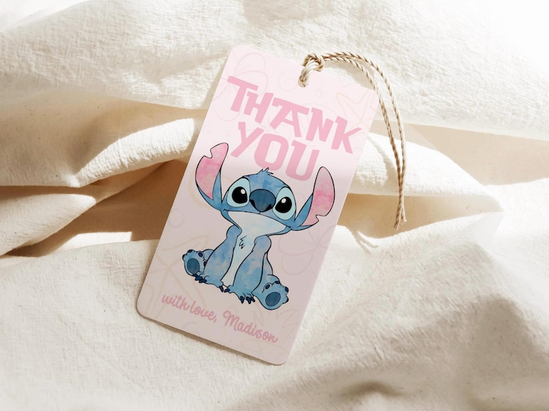 Puede incluir: Una etiqueta de regalo rosa con una ilustraci&oacute;n de un personaje de dibujos animados azul y las palabras "THANK YOU" en rosa. La etiqueta tambi&eacute;n incluye el texto "with love, Madison" en cursiva y est&aacute; sujeta a una cuerda de hilo natural.