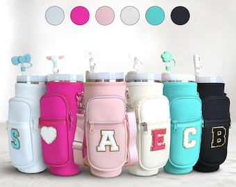 Puede incluir: Una colección de portabotellas de agua aisladas en varios colores, que se asemejan a bolsas de golf en miniatura. Cada portabotellas presenta una letra diferente, un pequeño bolsillo lateral y una correa para el hombro. Los colores incluyen blanco, rosa, rosa claro, blanco roto, turquesa y negro.