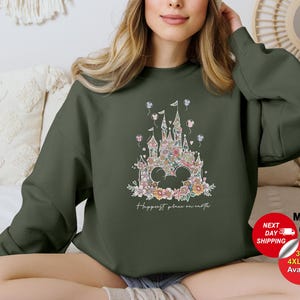 Puede incluir: Una sudadera verde con un dise&ntilde;o de castillo floral y el texto "Happiest place on earth".