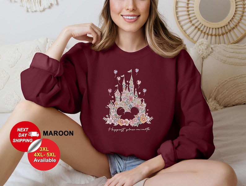 Puede incluir: Sudadera color granate con un dise&ntilde;o floral del castillo de Cenicienta y el texto "Happiest place on earth".