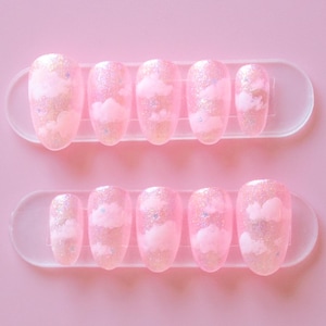 May include: Set of ten oval-shaped pink press-on nails with a white cloud design and iridescent glitter.