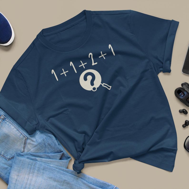 May include: A navy blue t-shirt with a white graphic of a magnifying glass over a question mark and the text "1+1+2+1".
