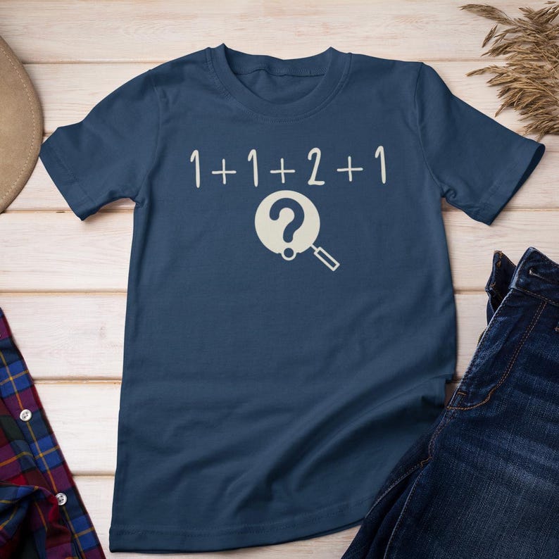 May include: A navy blue t-shirt with the text "1+1+2+1" and a magnifying glass with a question mark inside.