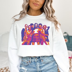 May include: White sweatshirt with a graphic print of a group of people in a colorful, stylized design. The people are wearing casual clothing and are standing in a row. The graphic is in shades of pink, purple, and orange.