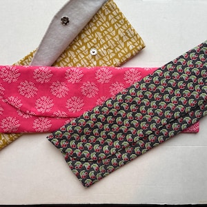 May include: Three fabric pouches with different patterns. One pouch is yellow with a white geometric pattern, another is pink with a white floral pattern, and the last is black with a red cherry pattern.