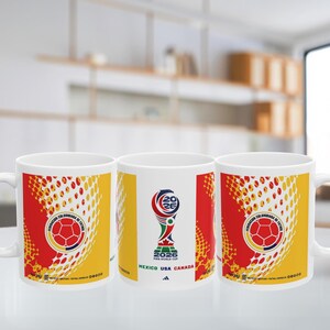 May include: White ceramic mug featuring the Colombian Football Federation logo and a soccer ball design. The mug also displays the FIFA World Cup 2026 logo with the text "MEXICO USA CANADA". The design incorporates red, yellow, and white colors.