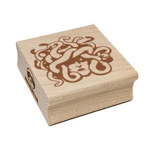 May include: A wooden stamp with a brown illustration of intertwined snakes. The stamp has a square shape and a light wood finish. The stamp also has a small logo on the side.