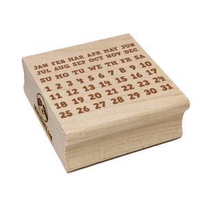 May include: A wooden calendar stamp with months, days of the week, and dates from 1 to 31 printed in brown ink. The stamp has a rounded edge and a logo on the side. The text includes "JAN FEB MAR APR MAY JUN" and "JUL AUG SEP OCT NOV DEC".
