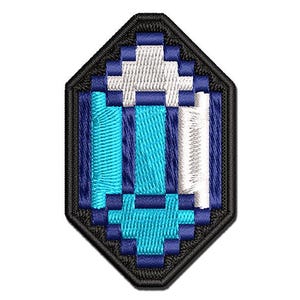 May include: Embroidered patch featuring a pixelated blue gem design. The gem has a white center and is outlined in black. The patch is a diamond shape, perfect for adding to clothing or accessories.