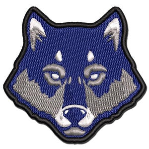 May include: An embroidered patch featuring the head of a wolf in shades of deep blue, silver, and white. The design is outlined with a thick black border, showcasing detailed stitching that defines the ears, eyes, snout, and fur texture.