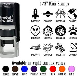 May include: A black and gray self-inking stamp with the text "trodat printy 4612" on it. The stamp is surrounded by a grid of 12 different space-themed images, each with a unique code. The text "1/2" Mini Stamps" is at the top of the grid. Below the grid, the text "Available in eight fun ink colors" is displayed with eight colored circles representing the ink colors: black, brown, blue, purple, green, red, orange, and pink.