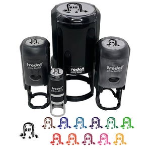 May include: A collection of black self-inking stamps with a tombstone design and the letters "RIP". The stamps are in various sizes, with the brand name "Trodat" visible. Below the stamps are several colored tombstone designs.