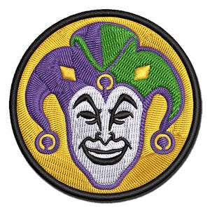 May include: A circular embroidered patch featuring a jester face with a white mask, black facial features, and a three-pointed hat in alternating purple and green colors. The background is yellow, and the entire design is bordered by a black edge.
