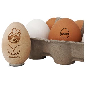 May include: A wooden egg-shaped Snigglesloth figurine with a sloth face design, next to a carton of eggs. One brown egg is labeled "JUMBO". The carton contains white and brown eggs. The Snigglesloth figurine has the text "SNIGGLESLOTH" at the bottom.