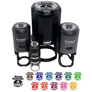 May include: A collection of black self-inking stamps with the text "MISSING HOMEWORK" and a dog graphic. The stamps are in various sizes, with several ink color options displayed below. The brand name "trodat" is visible on the stamps.