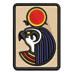May include: A rectangular embroidered patch featuring a stylized falcon head in profile, colored in black, white, and blue, topped with a red sun disk outlined in yellow. The design is set against a tan background with a thick black border.
