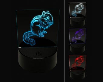May include: A 3D illusion lamp featuring a clear acrylic panel with an etched chipmunk design. The lamp sits on a round black base with a power button. The chipmunk graphic illuminates in various colors including cyan, blue, purple, and red.