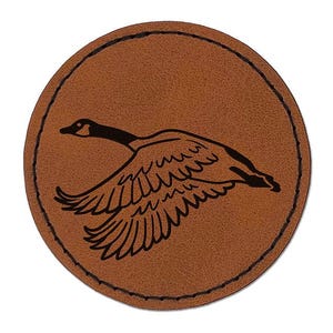 May include: A brown leather coaster with a black silhouette of a goose in flight.