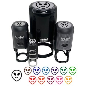 May include: A collection of black self-inking stamps with an alien face design. The stamps are in various sizes, with the brand name "trodat" visible. Below the stamps are several alien face designs in different colors.