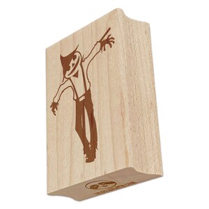 May include: A wooden stamp featuring a brown illustration of a scarecrow with a hat, suspenders, and outstretched arms. The stamp has a curved top and a logo at the bottom. The scarecrow design is detailed and stylized.