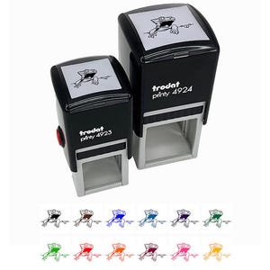 May include: Two black self-inking rubber stamps with a cartoon image of a lizard. The larger stamp says "trodat printy 4924" and the smaller stamp says "trodat printy 4923". The stamps are shown against a white background. Below the stamps are ten different colored images of the lizard.