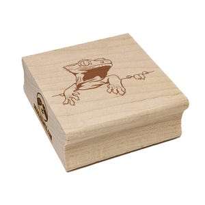 May include: A wooden stamp featuring a detailed brown illustration of a gecko. The gecko is positioned as if it's climbing, with its claws and body visible. The stamp has rounded edges and the text "CHARLESCRAFTS.COM" is printed on the side.