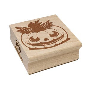 May include: A wooden stamp featuring a smiling jack-o'-lantern with a crow perched on top. The stamp has a light brown color and is designed for crafting and Halloween projects. The website address is printed on the side.