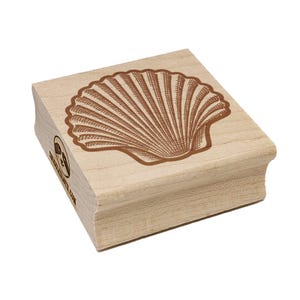 May include: A wooden stamp featuring a detailed brown seashell design. The stamp is rectangular with a curved edge and a logo on the side. The seashell illustration is centered on the top surface.